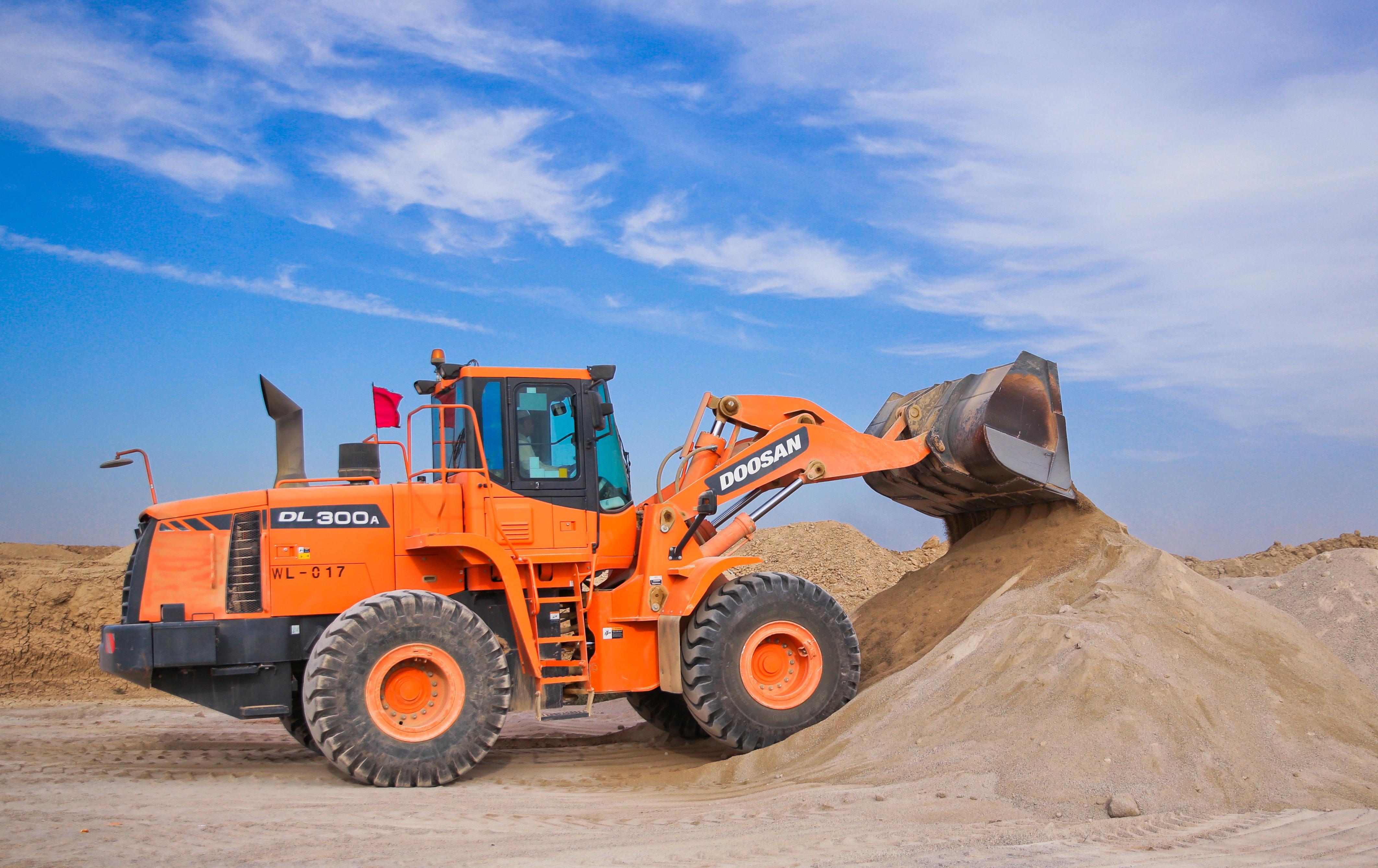 A large orange tractor is digging sand.